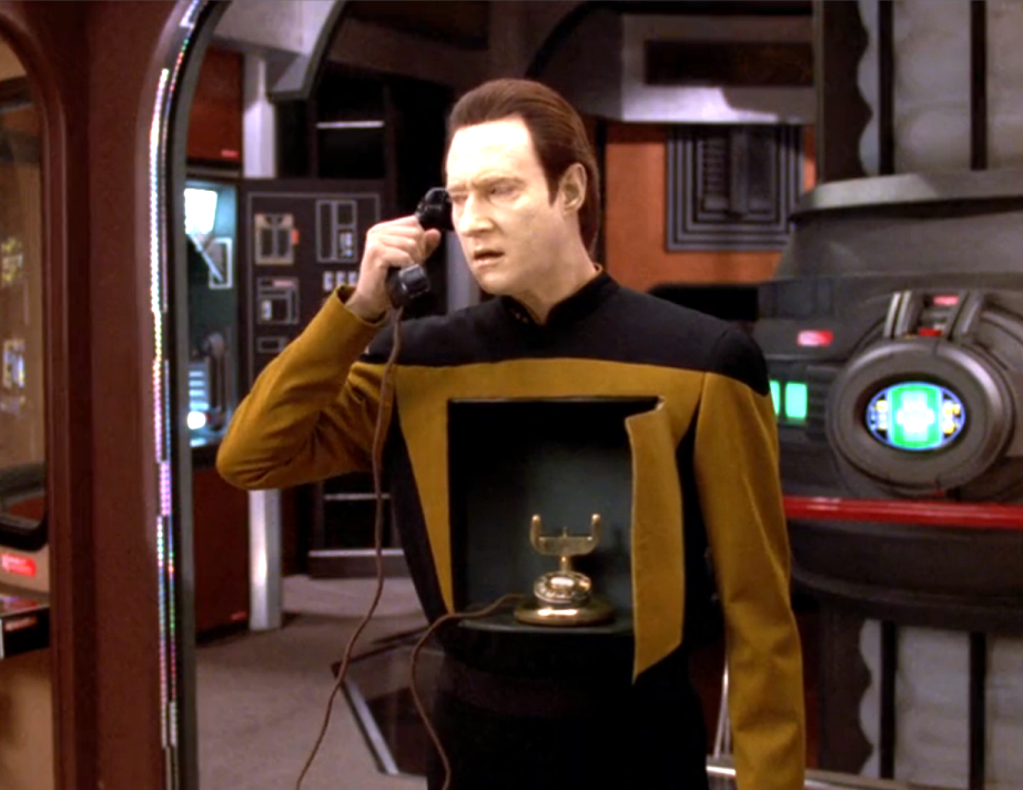 Data speaking into an old-style telephone that is sitting in a compartment in his chest