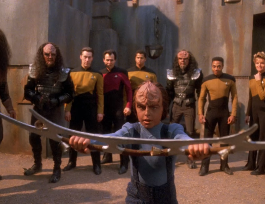 Alexander brandishing a bat'leth with several Klingon and Starfleet onlookers