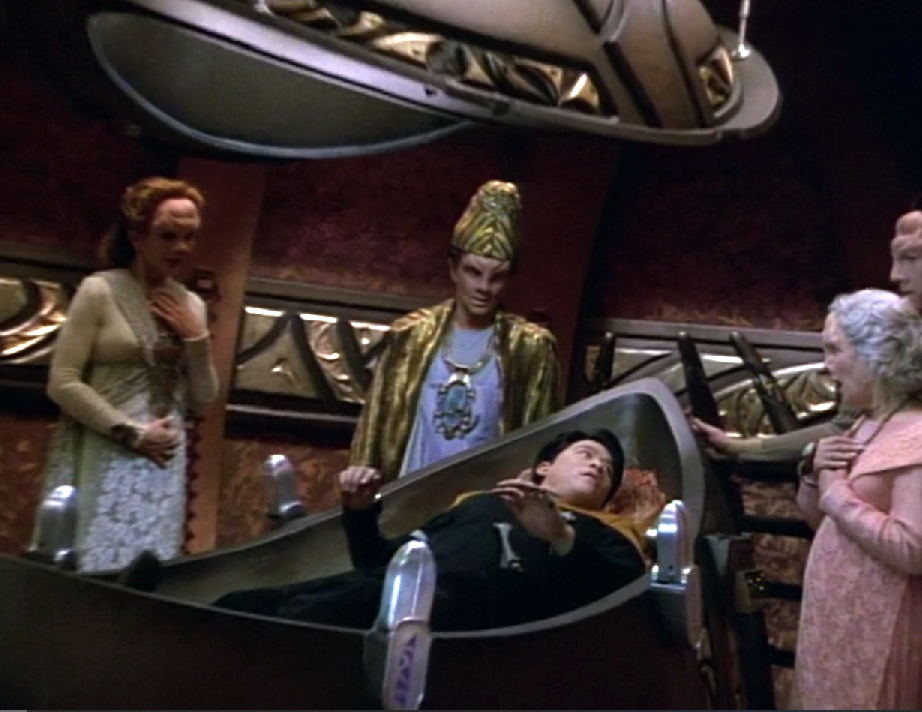Harry Kim lying in some sort of pod with several people standing around him looking shocked
