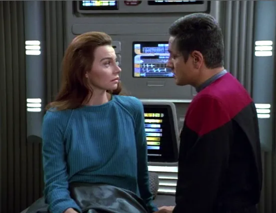 Seska lying on a bed in sickbay talking to Chakotay