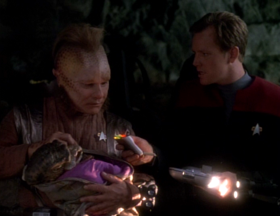 Neelix holds an alien infant while Paris scans it with his tricorder