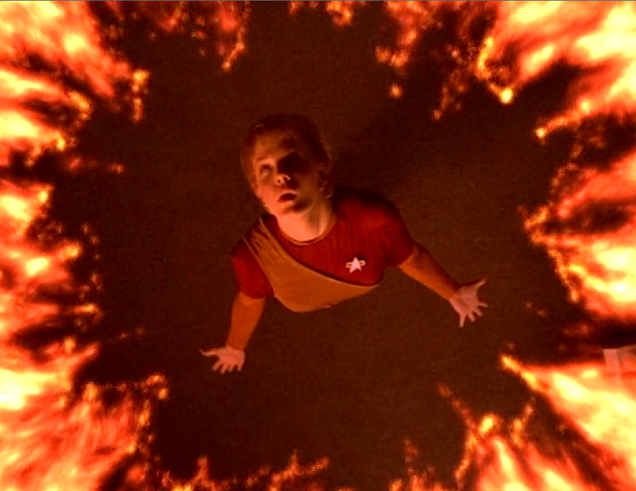 A downward camera angle showing Kes looking up, with arms outstretched, and surrounded by a ring of fire