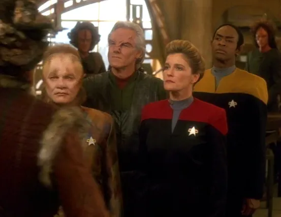 Janeway, Tuvok, and Neelix standing with several Kazon and Trabe in a conference room