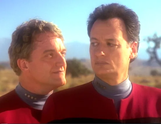 John de Lancie as Q, and another Q, wearing Starfleet uniforms and standing in a desert