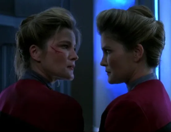 Two Captains Janeway, one with a scar below her right eye, discuss strategy next to the warp core