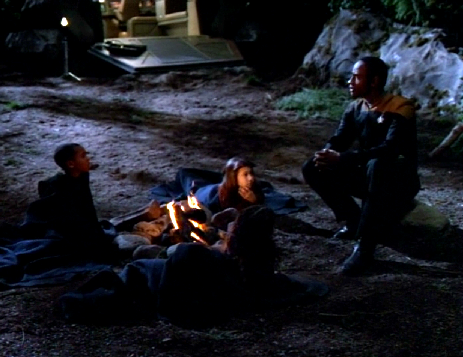 Tuvok and three children sitting around a campfire outside at night
