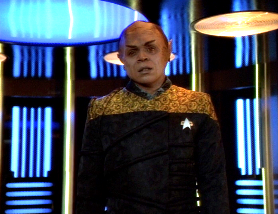 A strange-looking half-Vulcan half-Talaxian man stands on the transporter pad