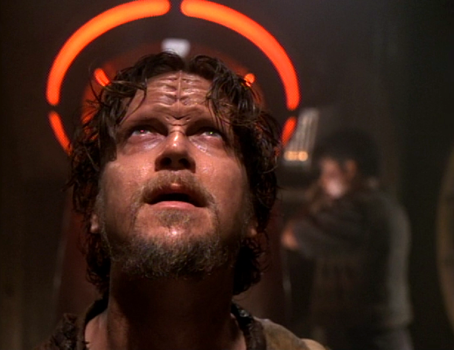 A goateed man looking upward, his head haloed by the red glow of a chute that Harry is working on in the background
