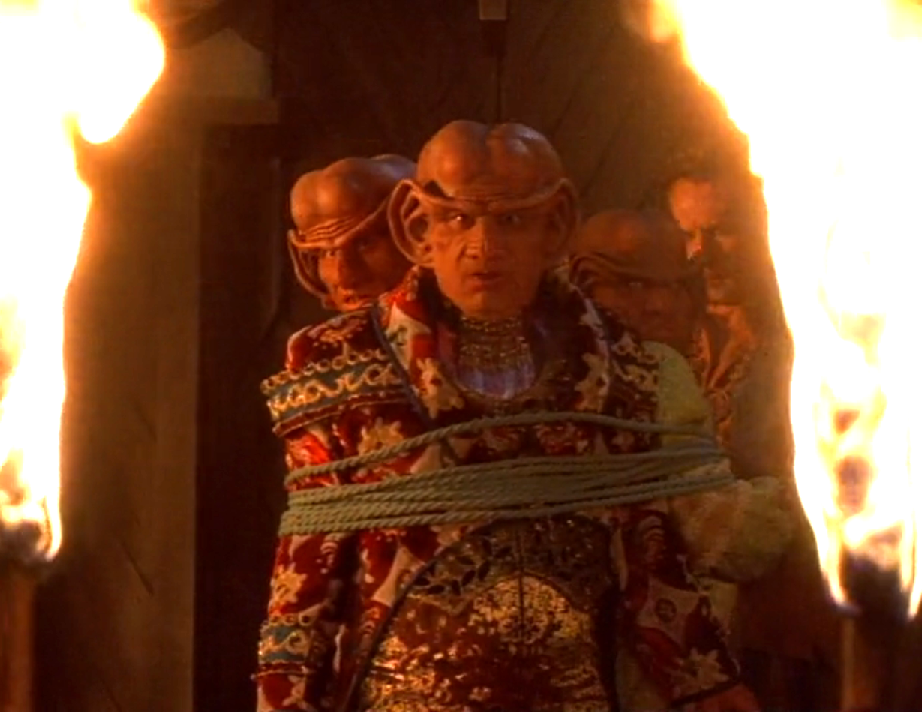 Three Ferengi looking concerned as they are tied up and threatened with torches