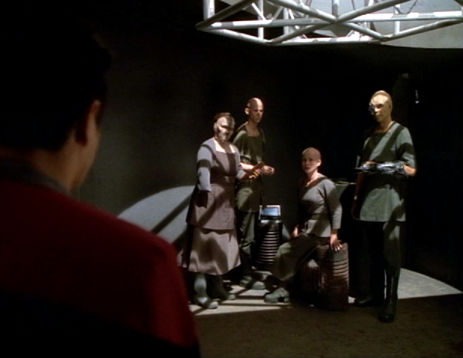 Chakotay approaching four bald colonists with missing or artificial limbs