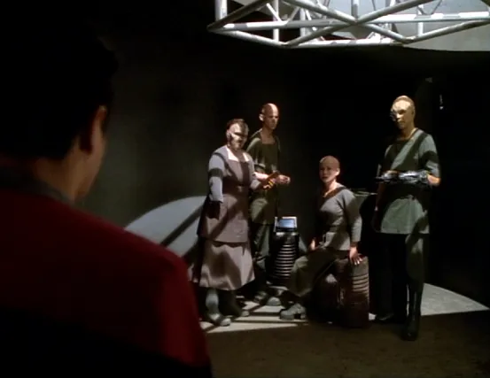 Chakotay approaching four bald colonists with missing or artificial limbs