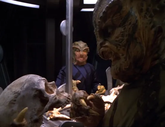 Two reptile-like aliens examining a skull and other bones