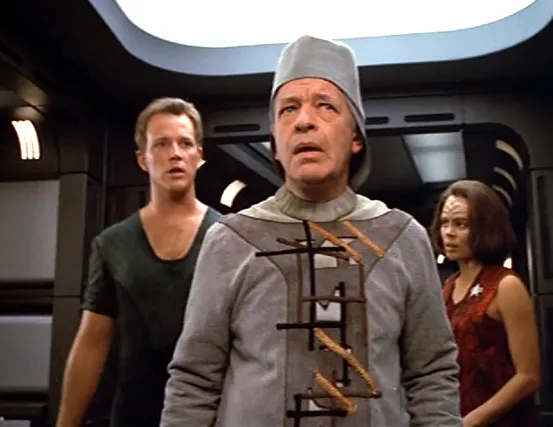 Tom, B'Elanna, and a confused looking man in one of Voyager's corridors