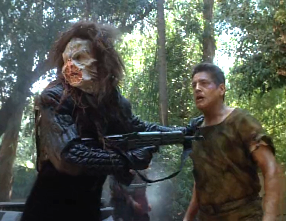 A scary looking alien holding back Chakotay with a rifle