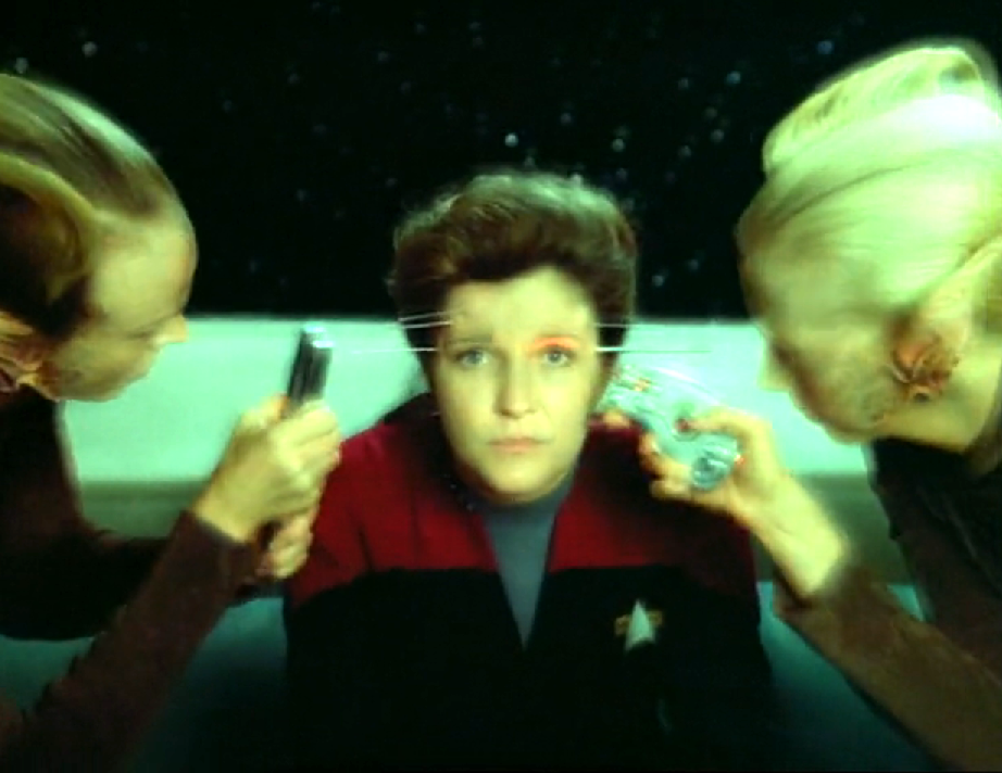 Janeway with several needles protruding from her temples as two aliens scan her