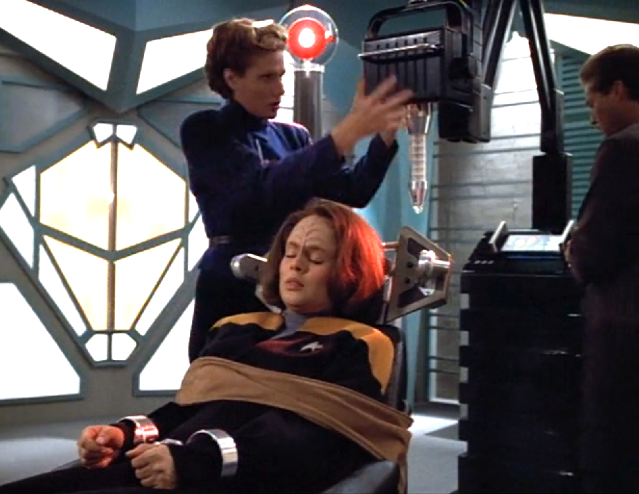 An unconscious B'Elanna strapped to a chair as another woman prepares an intimidating medical device
