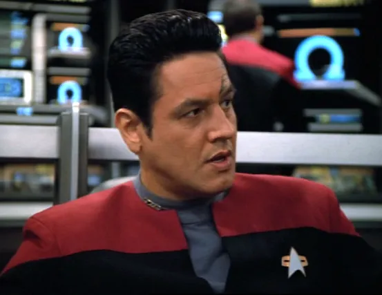 Chakotay looking concerned as the bridge monitors all around him display the Greek letter Omega