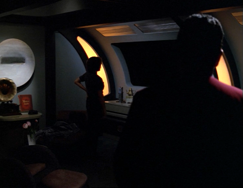Chakotay and Janeway standing in a darkened room, with Janeway staring out the window into a black abyss with no stars