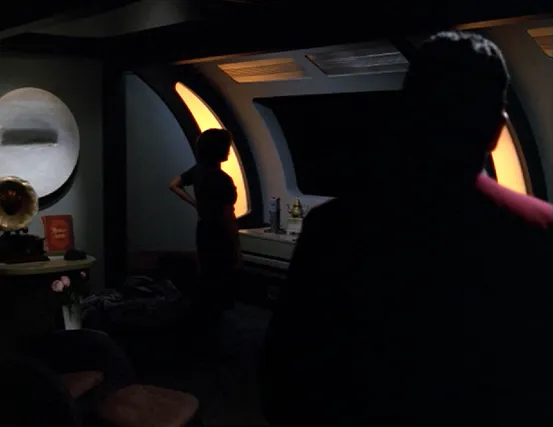 Chakotay and Janeway standing in a darkened room, with Janeway staring out the window into a black abyss with no stars