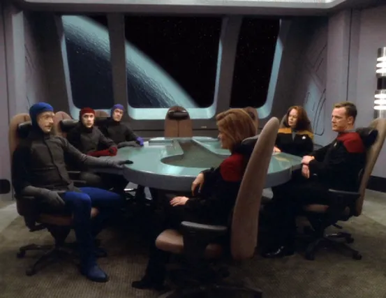 Three aliens sitting in the conference room with Janeway, Paris, and Torres. Outside the window is a planet-sized sphere of water