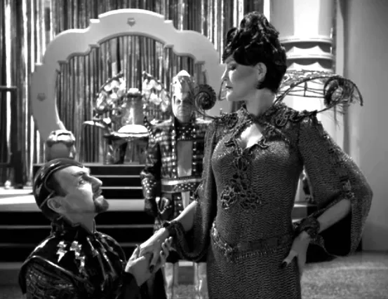A black-and-white scene with a man kneeling before Janeway, who is wearing an elaborate dress