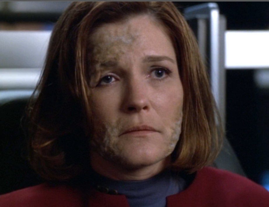 A close-up of Captain Janeway, who has strange gray markings on her forehead and cheeks