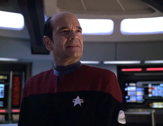 The Doctor wearing a red uniform and captain's pips on the bridge of Voyager