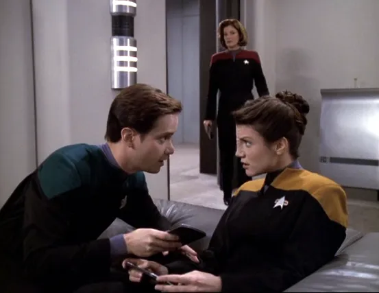 Two low-ranking crewmembers talking in the mess hall as Janeway is entering