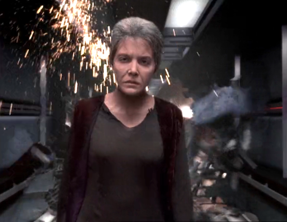 An aged and tired-looking Kes walking down a corridor as the bulkheads twist and explode behind her