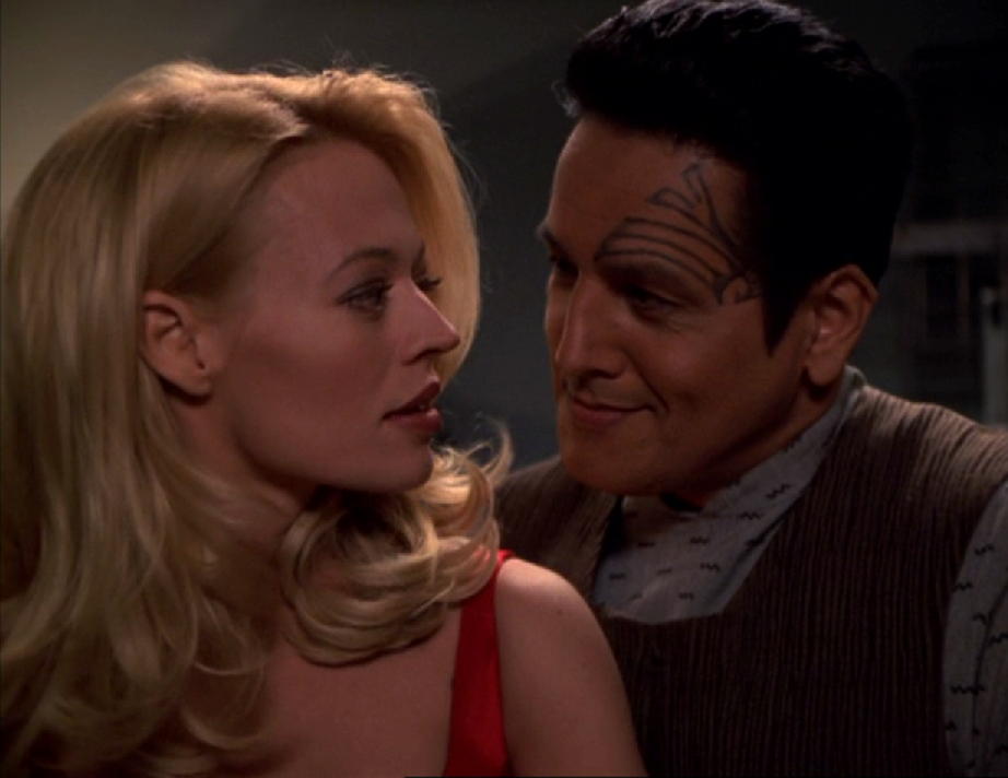 Seven and Chakotay looking at each other lovingly. He's in a casual suit, she's wearing a red dress and has let her hair down