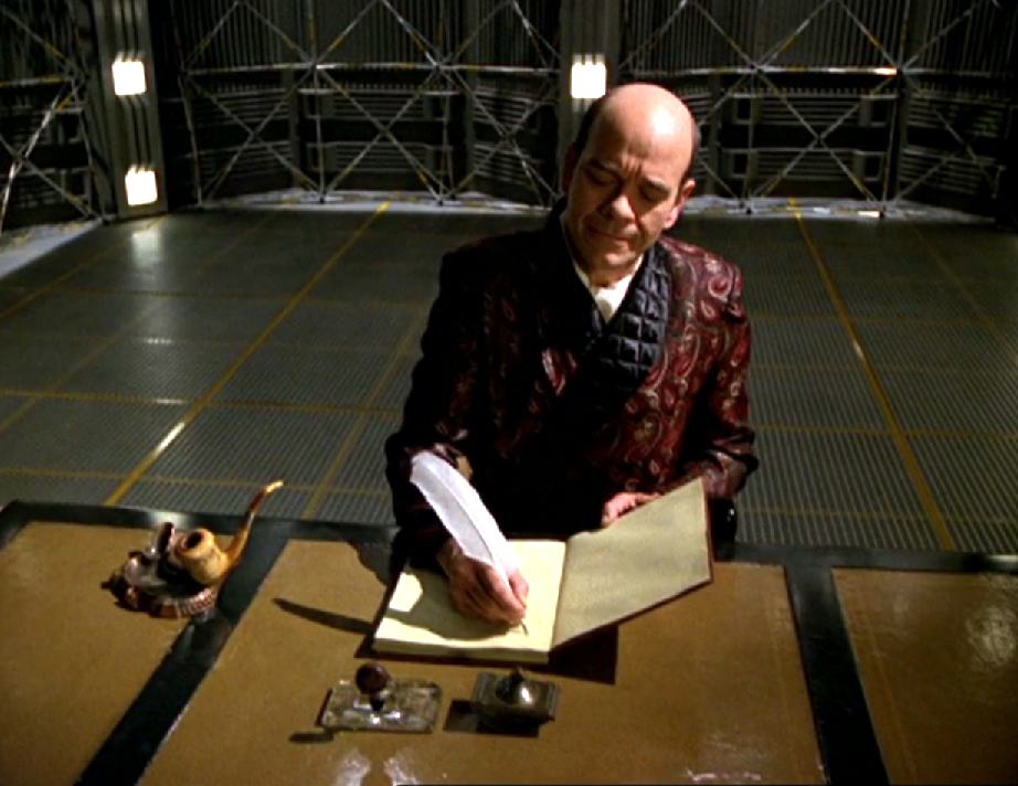 The Doctor, wearing a smoking jacket and writing in a book with a quill