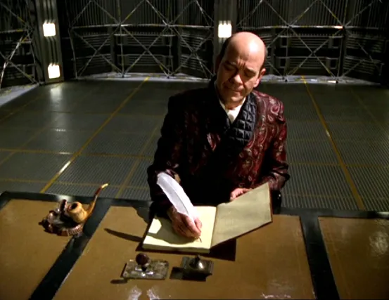 The Doctor, wearing a smoking jacket and writing in a book with a quill