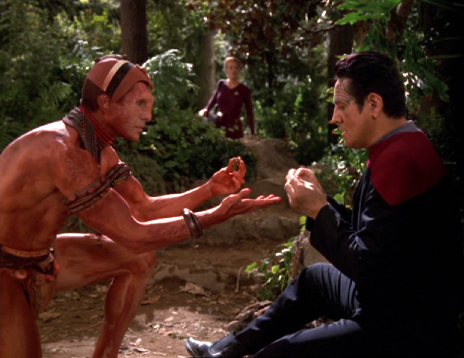Chakotay communicating with a primitive local on a planet as Seven watches