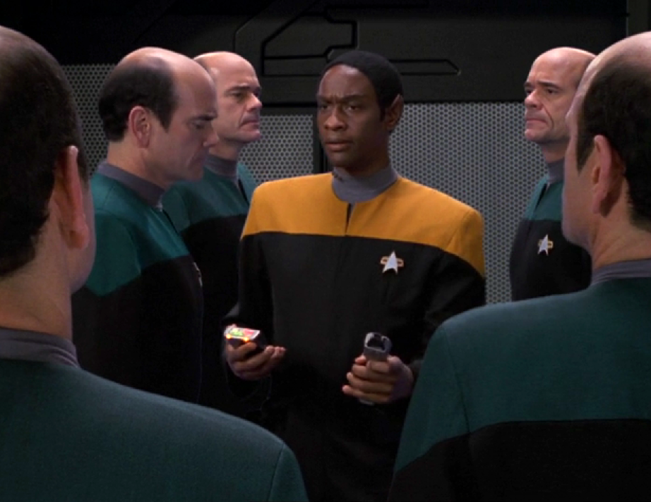 Tuvok, holding a tricorder and a phaser, in a room with numerous copies of the Doctor