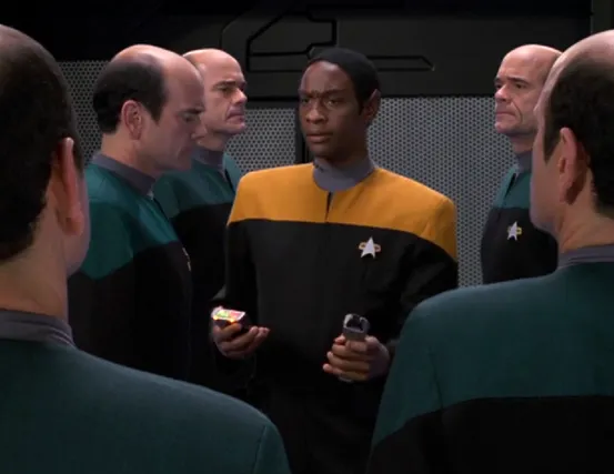 Tuvok, holding a tricorder and a phaser, in a room with numerous copies of the Doctor