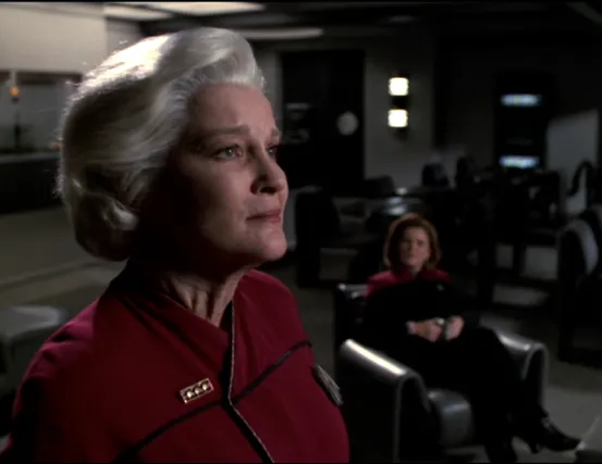 An aged Admiral Janeway gazing through the windows of the mess hall while the younger Captain Janeway watches